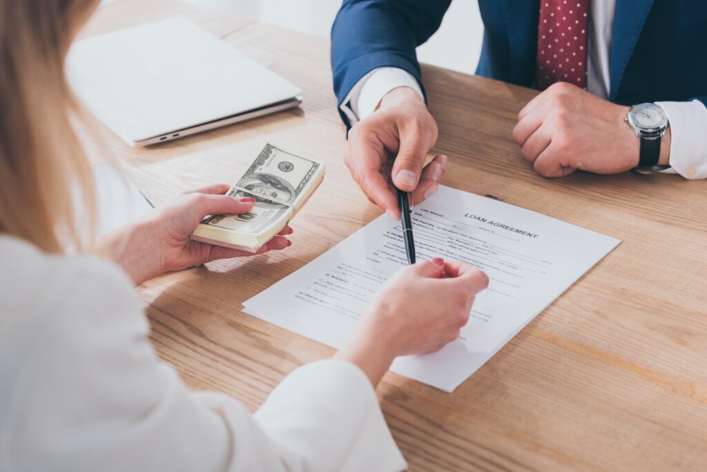 cropped shot of businessman pointing at signature place in loan agreement near woman holding dollar