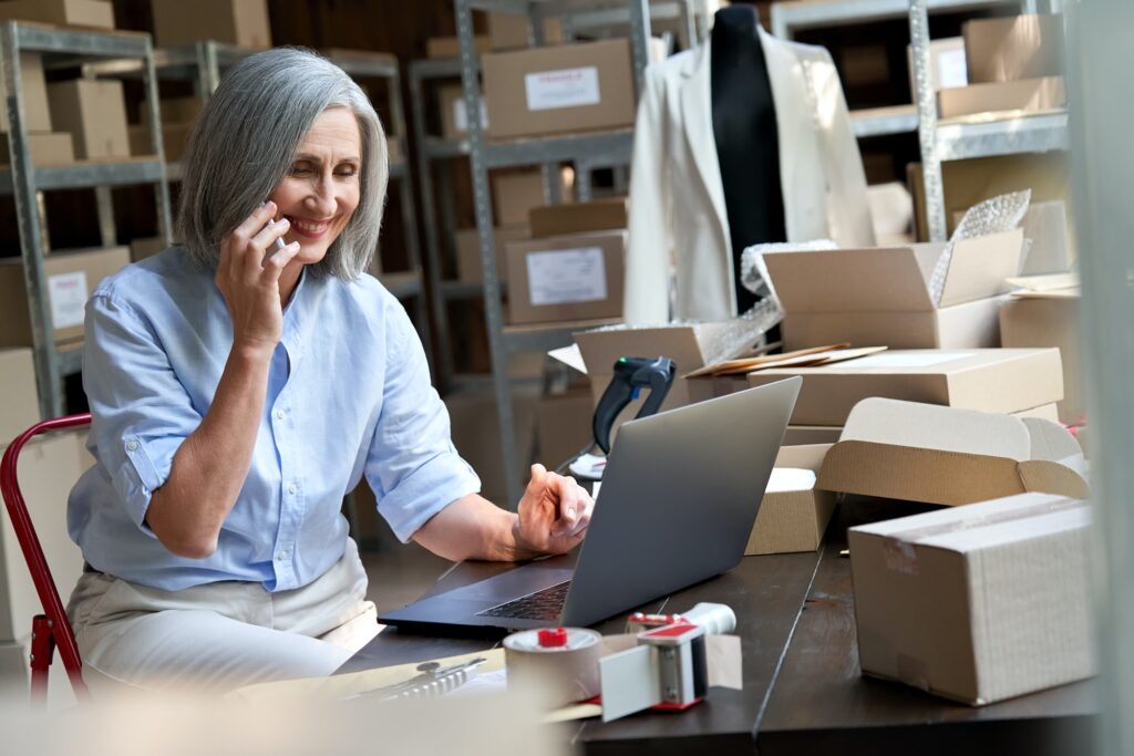 Female dropshipping business owner using laptop talking on phone at work.