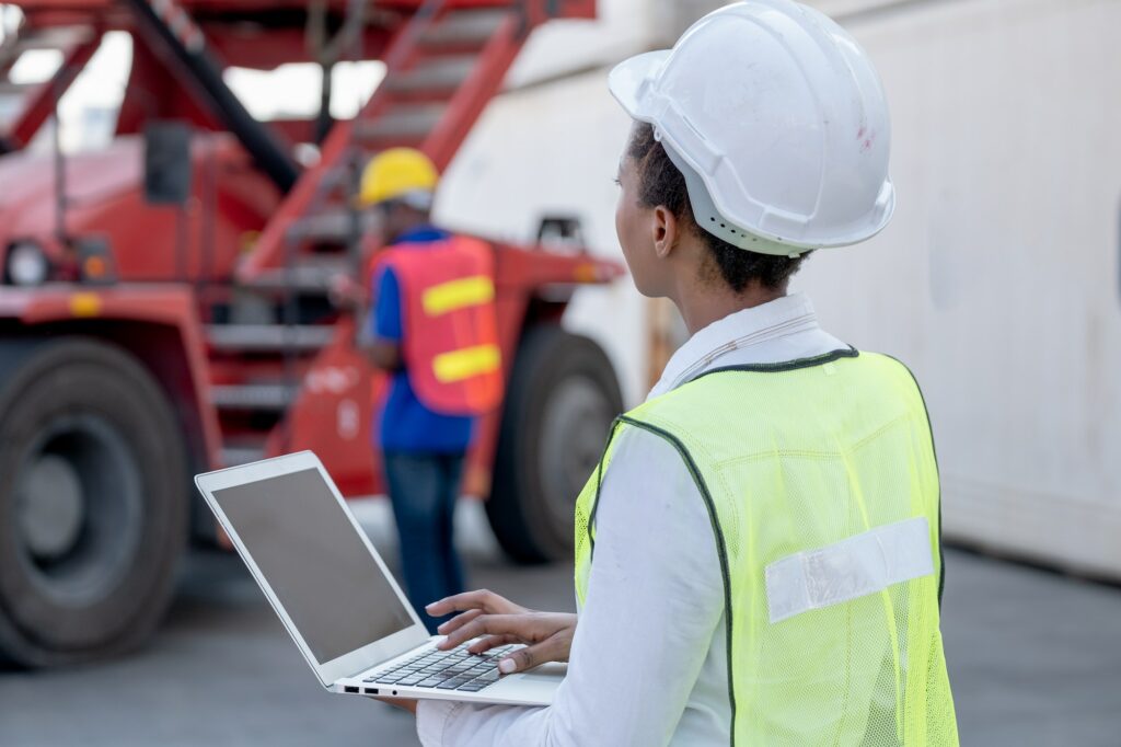 American African technician worker woman typing and look to truck while her co-worker work