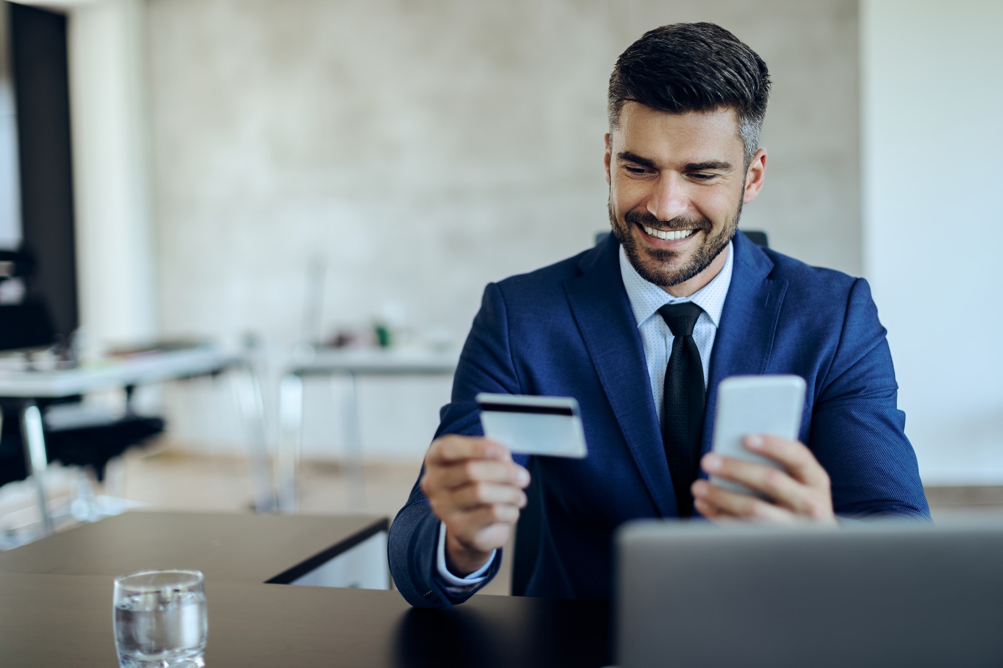 Happy entrepreneur online banking with credit card and mobile phone in the office.